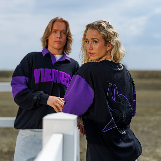 Two models wearing the Rugby Shirt and Two-Tone Lax Tee in black and purple at a fence