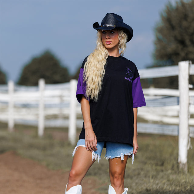 Model wearing the Two-Tone Lax Tee in black and purple with a black cowboy hat, full-length view