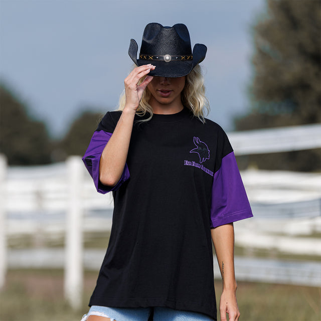 Model wearing the Two-Tone Lax Tee in black and purple with a black cowboy hat, front view