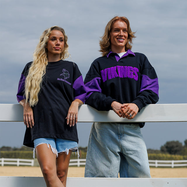 Two models wearing the Rugby Shirt and Two-Tone Lax Tee in black and purple at a fence