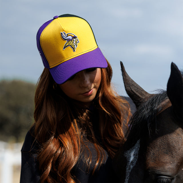 Model wearing the Colour Block New Era Snapback in gold and purple beside a horse