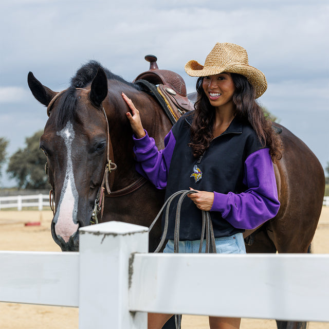 Model wearing the Two-Tone 1/4 Zip Pullover in black and purple beside a horse
