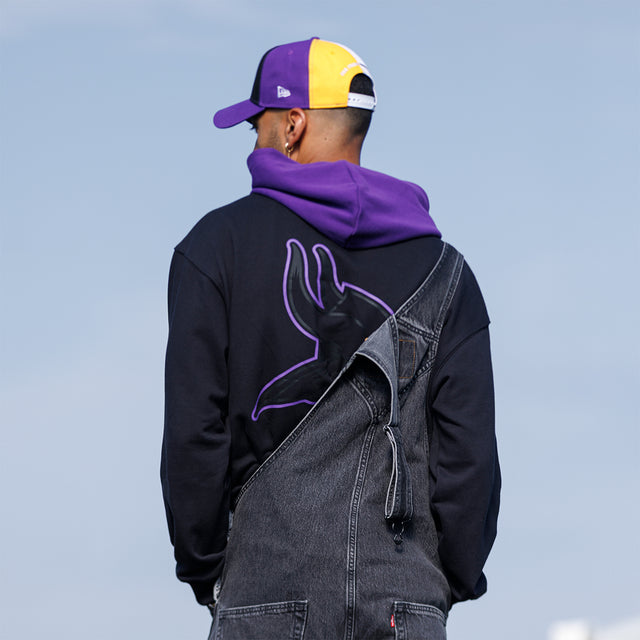 Model wearing the Two-Tone Hoodie in black and purple with a Vikings cap, back view