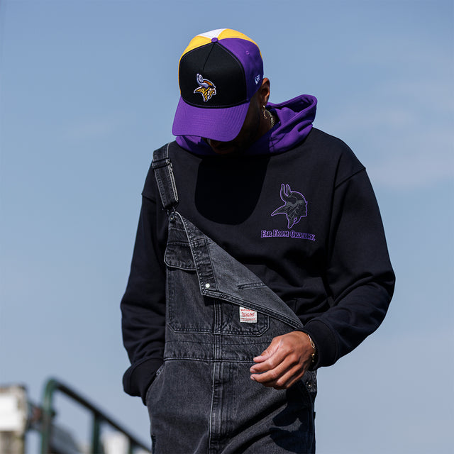 Model wearing the Two-Tone Hoodie in black and purple with a Vikings cap, front three-quarter view